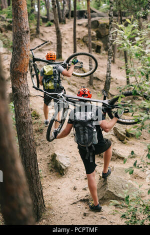 Vista posteriore della prova i motociclisti che trasportano le moto sulle spalle al forest Foto Stock