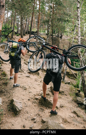 Vista posteriore della prova i motociclisti che trasportano le moto sulle spalle alla foresta e in salita Foto Stock