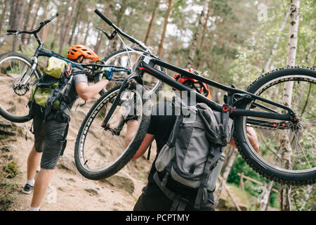 Vista posteriore del giovane biker di prova che trasportano le moto sulle spalle alla foresta e in salita Foto Stock