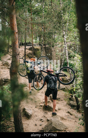 Prova di giovani motociclisti che trasportano le moto sulle spalle alla foresta e in salita Foto Stock