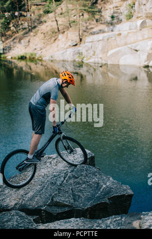 Prova atletica biker bilanciamento sulla scogliera di roccia sopra il lago Foto Stock