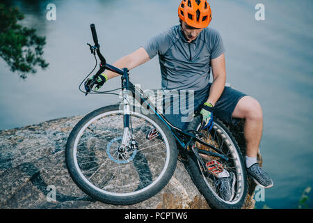 Prova di giovani biker rilassante sulla scogliera rocciosa su acqua con noleggio biciclette Foto Stock