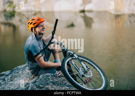 Sorridente prova giovani biker rilassante sulla scogliera rocciosa su acqua Foto Stock