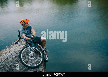 Bel giovane biker prova rilassante sulla scogliera rocciosa su acqua Foto Stock