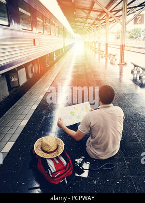 Viaggiatore seduto e guardando la mappa in una stazione ferroviaria. Concetto di viaggio con contrasto elevato Foto Stock