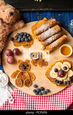 Colazione per bambini. Frittelle con le bacche e guerrieri, con facce allegre. Vista superiore Foto Stock