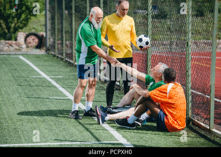 Interracial anziani giocatori di calcio si stringono la mano dopo la partita sul campo verde Foto Stock