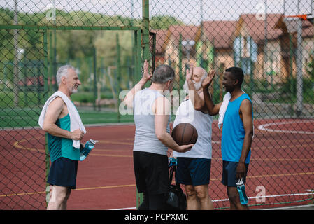 Gruppo di multirazziale vecchio sportivi con basket ball dando alta cinque di ogni altro sul parco giochi Foto Stock