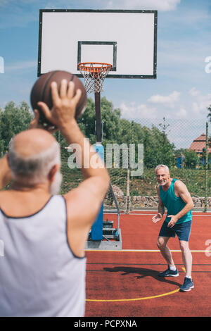 Uomini anziani giocare a basket insieme sul parco giochi sul giorno di estate Foto Stock