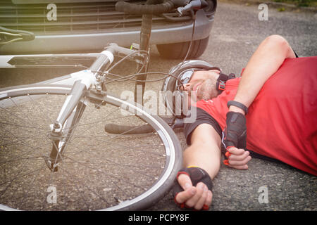 Ciclista giacente sulla strada dopo un incidente che coinvolge un auto e biciclette Foto Stock