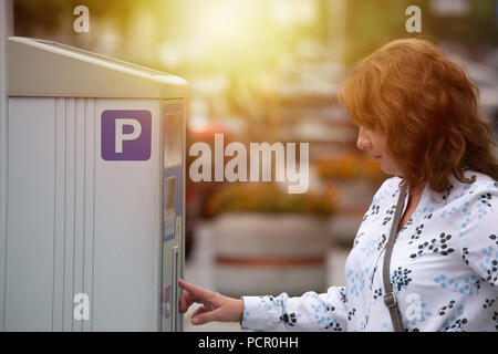 Donna che utilizza un parchimetro in zona parcheggio area in una città Foto Stock