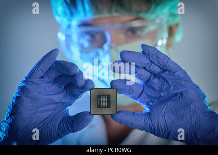 Un ingegnere che lavora in un laboratorio indossando una speciale uniforme e guanti protettivi detiene il nuovo processore in mani e lo esamina Foto Stock