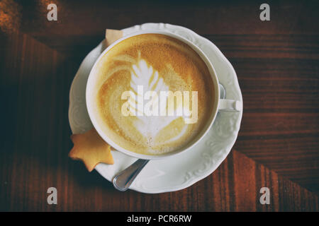 Bella tazza di porcellana di caffè con cappuccino arte con poco cookie su una piastra Foto Stock