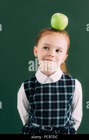 Sorridente pensieroso little schoolgirl con Apple sulla testa guardando lontano Foto Stock