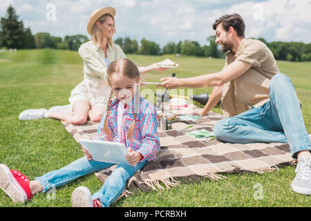 Grazioso fanciullo utilizzando digitale compressa durante il riposo con i genitori al picnic Foto Stock