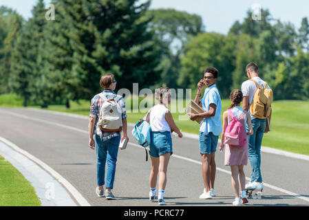 Vista posteriore del multietnica amici adolescenti con libri e zaini camminare insieme in posizione di parcheggio Foto Stock