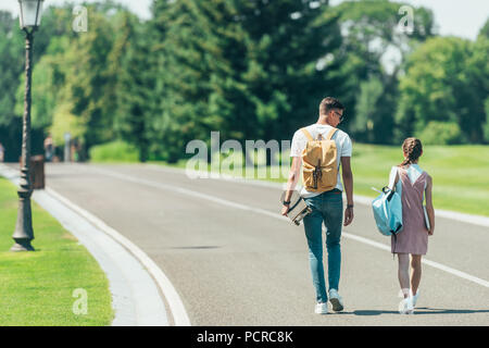 Vista posteriore del ragazzo adolescente e una ragazza con zaini e skateboard camminare insieme in posizione di parcheggio Foto Stock