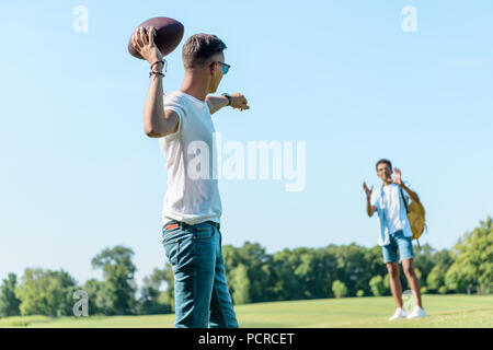 Multietnica ragazzi adolescenti giocando con il pallone da rugby in posizione di parcheggio Foto Stock