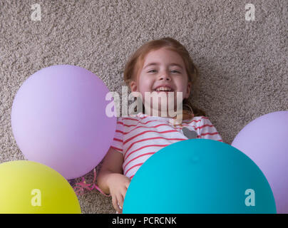 Ragazza con palloncini, bambino con palloncini, bambino con palloncini sdraiato sul pavimento. Ragazza è esprimere la creatività e guardando la telecamera e sorridente. Foto Stock