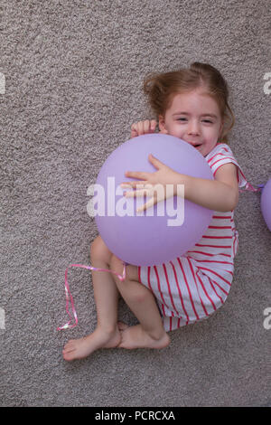 Ragazza con palloncini, bambino con palloncini, bambino con palloncini sdraiato sul pavimento. Ragazza è esprimere la creatività e guardando la telecamera e sorridente. Foto Stock