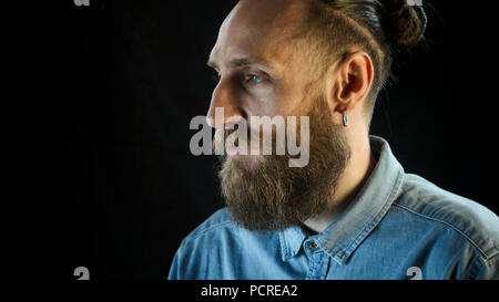 Ritratto di uomo barbuto in una blu denim Shirt su sfondo nero. Foto Stock