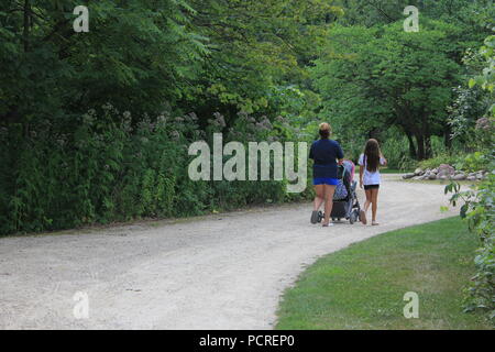Donna che spinge un passeggino e prende sua figlia per una passeggiata sul sentiero natura nei boschi. Foto Stock