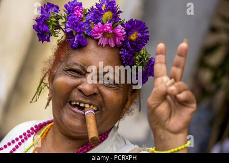 Segno di pace, vecchia donna cubana con decorazioni floreali e sigaro in posa per i turisti per ricevere un suggerimento, La Habana, Havana, La Habana, Cuba, Cuba Foto Stock