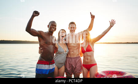 Ridendo gruppo di amici spensierato in piedi a braccetto insieme in un lago divertendosi in un tardo pomeriggio estivo Foto Stock