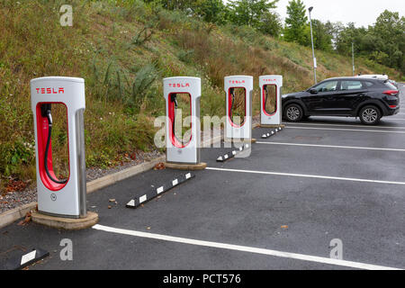 SARN, Regno Unito - 2 agosto 2018 : Una fila di Tesla sovralimentazioni accanto al parcheggio vuoto baie a Sarn Park servizi autostradali al di fuori della M4 vicino BRI Foto Stock