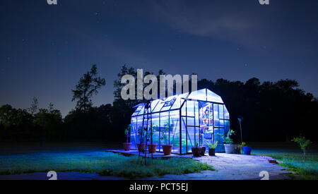 Le stelle e le nuvole nel cielo con un illuminato sotto serra Foto Stock