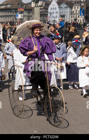 Donna sulla bicicletta di antiquariato, membri della Corporazione su la parata delle corporazioni, il Festival di Primavera di 'Sechseläuten', Old Town, Zurigo, Cantone di Zurigo, Svizzera Foto Stock