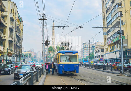 Alessandria, Egitto - 18 dicembre 2017: il blu brillante tram retrò in Mahta Raml al quadrato con minareto bianco di Al Qaed Ibrahim Mosque sul backgrou Foto Stock