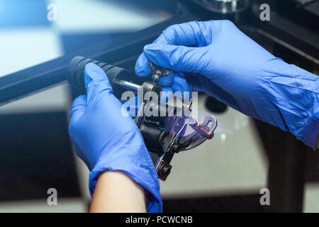 Le mani di un artista del tatuaggio in blu di guanti di gomma di tenere un dermografo. Salone di tatuaggi tema Foto Stock