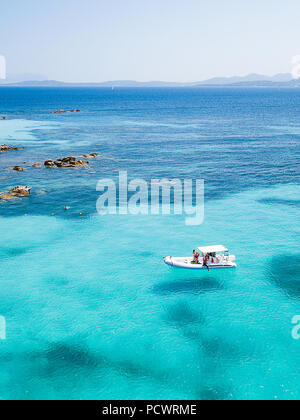 Vista da sopra, fotografia aerea di una barca con alcuni turisti rilassata a bordo dei galleggianti su un trasparente e acque turchesi del mar Mediterraneo. Costa Smeralda Foto Stock