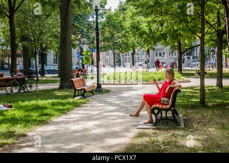 Donna in abito rosso seduta su una panchina nel parco Foto Stock