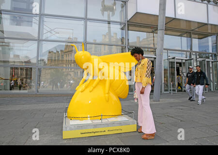 Manchester, Regno Unito, 3 agosto 2018. Una donna che indossa un giallo in alto si ferma accanto a un gigante giallo Ape. Il Manchester City Council e selvaggio circa arte stanno portando la comunità insieme con 'Bee nella città' che vede oltre a 1oo Bee Gigante sculture disegnate individualmente e disposto intorno alla città. Vi è un'applicazione interattiva per famiglie da utilizzare per trovare le api e sembra attrarre le famiglie a tutti gli angoli della città. Manchester, 4° agosto 2018 (C)Barbara Cook/Alamy Live News Foto Stock
