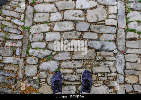 Coppia di piedi in scarpe su un vecchio sentiero acciottolato. Inizio di un nuovo viaggio. Foto Stock