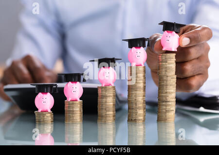 Close-up di persona d'affari immissione Piggybank con cappuccio di graduazione sulle monete impilate Foto Stock