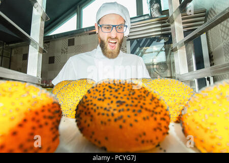 Giovani baker a urlare contro freschi panini caldi con semi di papavero in panetteria in background. Foto Stock