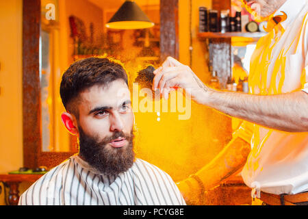Barbiere mette una polvere pennello sul cuoio capelluto di un giovane ragazzo bello con un baffi e barba. Uomini parrucchiere. Foto Stock