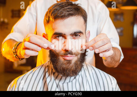 Barbiere fa un baffi di acconciatura per un giovane ragazzo bello in un maschio barbiere. Barbiere. Foto Stock