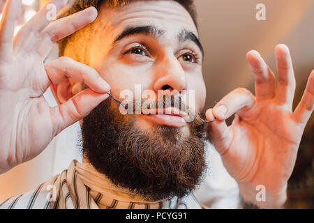 Barbiere fa un baffi di acconciatura per un giovane ragazzo bello in un maschio barbiere. Barbiere. Foto Stock