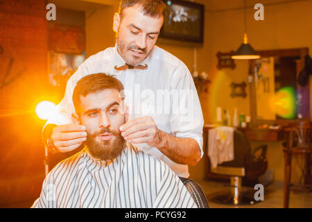 Barbiere fa un baffi di acconciatura per un giovane ragazzo bello in un maschio barbiere. Barbiere. Foto Stock