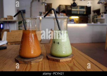 Due bicchieri (o "tubi") del Matcha Latte e ghiacciata Thai tè serviti in un bar. Foto Stock