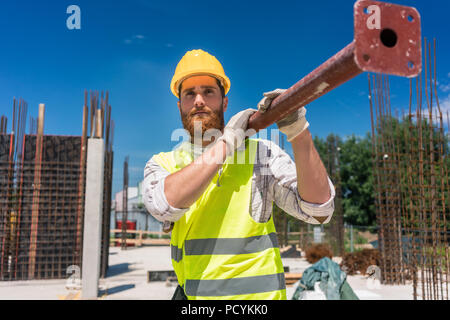 Colletto blu lavoratore portando una pesante barra metallica durante il lavoro Foto Stock