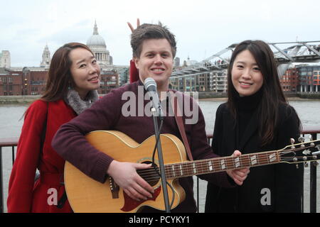 Due studenti coreani godere e divertirsi a Londra lungo gli argini del fiume Tamigi come musicista di strada suona con la cattedrale di St Paul in background Foto Stock