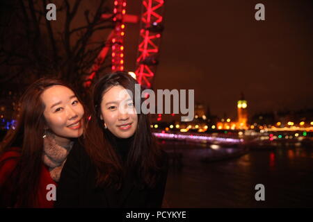 Due giovani amici Korean ladies godere di sera a Londra, foto con luminose Thames, London Eye, Westminster Bridge, Big Ben in background Foto Stock