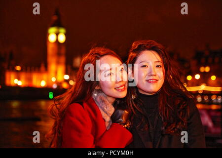 Due amici felice giovani donne coreane godetevi il tempo a Londra sulla riva del fiume Tamigi con Westminster Bridge e il Big Ben shining in background Foto Stock