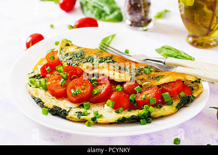 Frittata con pomodori, spinaci e cipolla verde sulla piastra bianca. Frittata - omelette italiano. Foto Stock