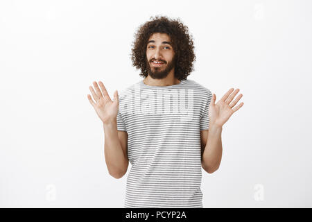 Incurante bello maschio modello di acconciatura afro e malati barba, alzando le palme in surrender e sorridente con nervosamente, rifiutando dall'offerta o richiesta Foto Stock
